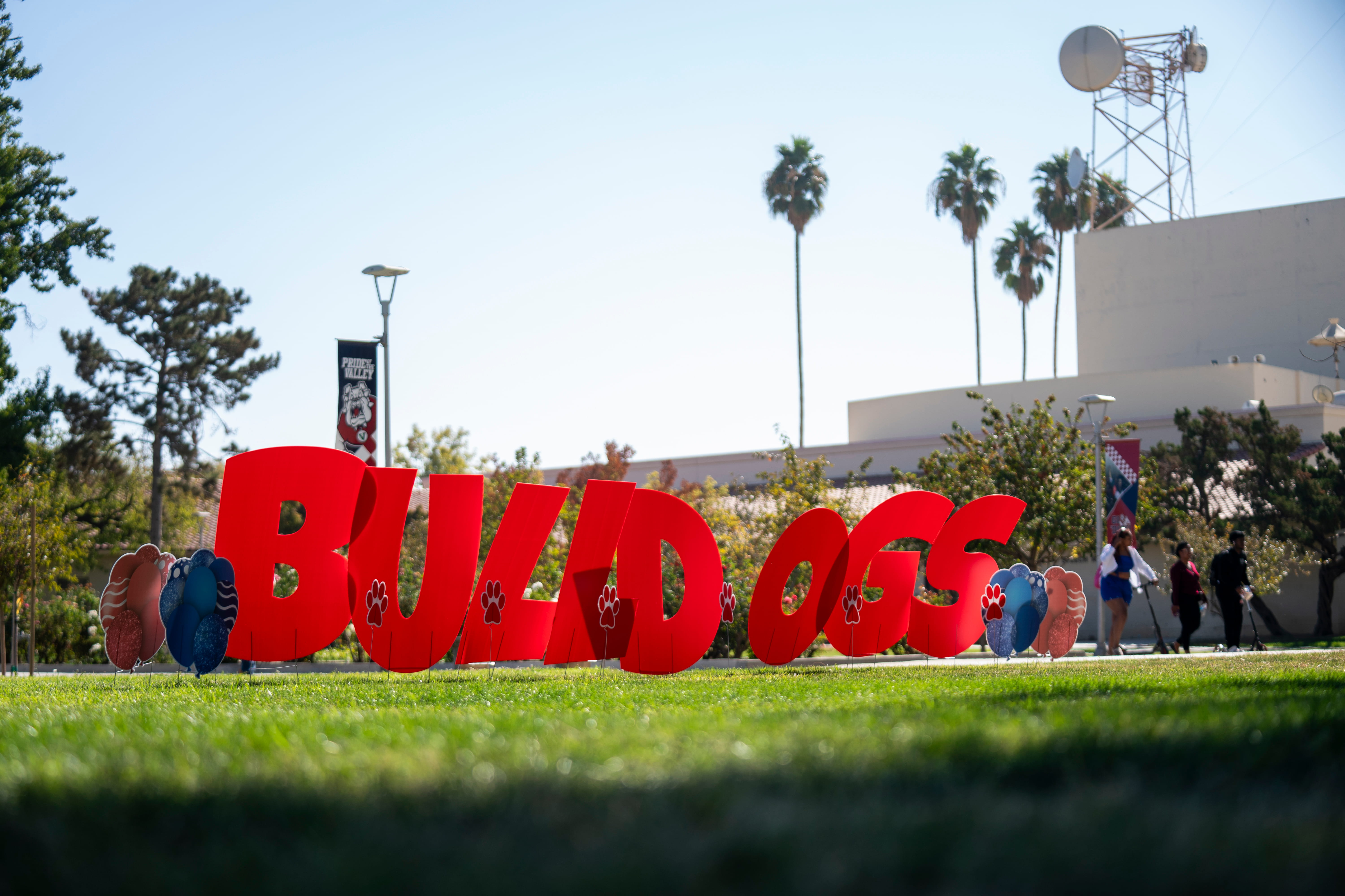 Large red letters spelling "BULLDOGS" displayed on a grassy lawn on the Fresno State campus, flanked by paw-print yard signs.